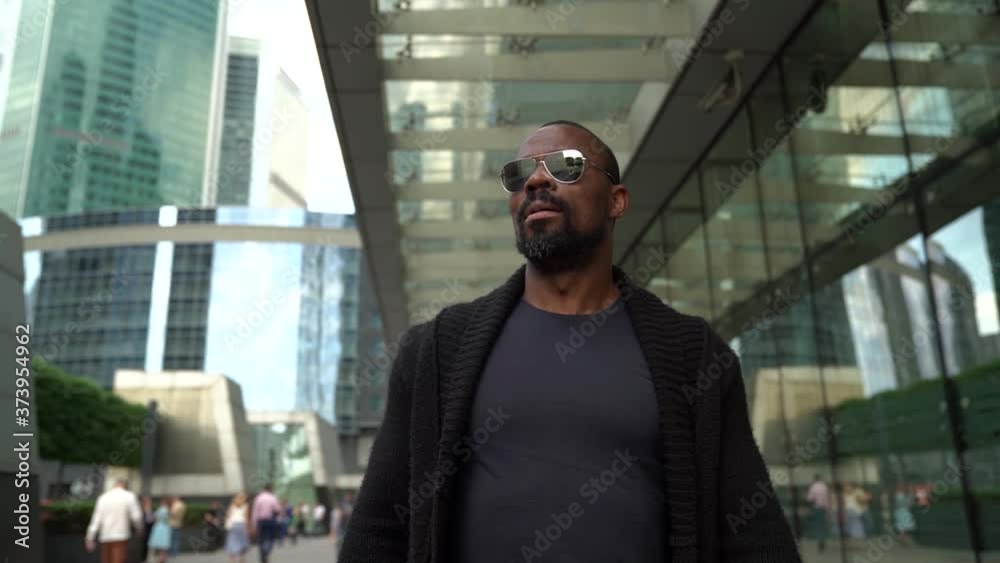 black male tourist is walking in downtown of modern city at sunny day, looking around black male tourist is walking in downtown of modern city at sunny day, looking around