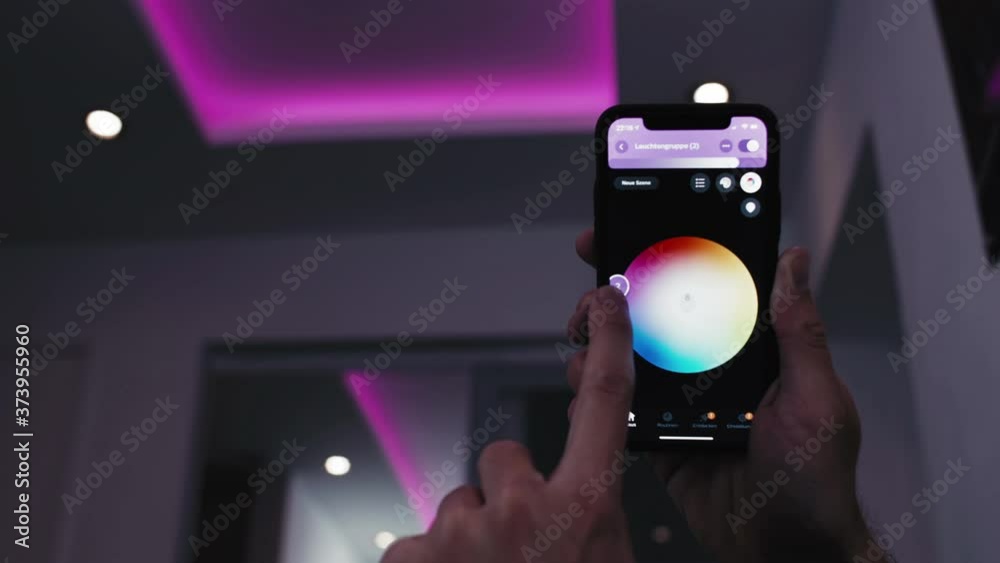 Low angle shot - A person on a Phone adjusting colored LED ceiling lights remotely  via wifi connection. Changing the colore randomly throughout the color spectrum.