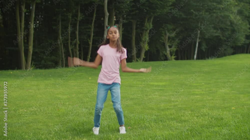 Lovely preadolescent african american girl with trendy hairstyle dancing hip-hop on green grass, making improvisation and moving to the groove happily, practicing street dance and freestyle outdoors. Lovely preadolescent african american girl with trendy hairstyle dancing hip-hop on green grass, making improvisation and moving to the groove happily, practicing street dance and freestyle outdoors.