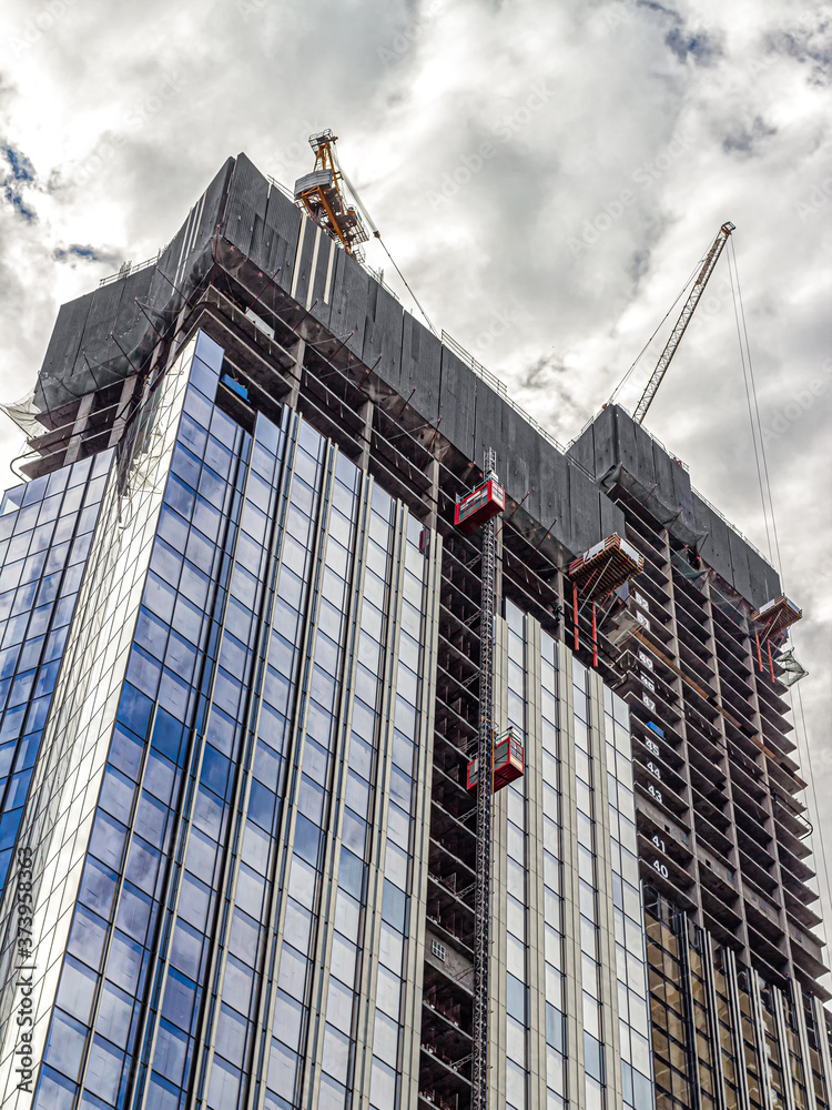 Skyscraper under construction with glass walls against a cloudy sky Skyscraper under construction with glass walls against a cloudy sky