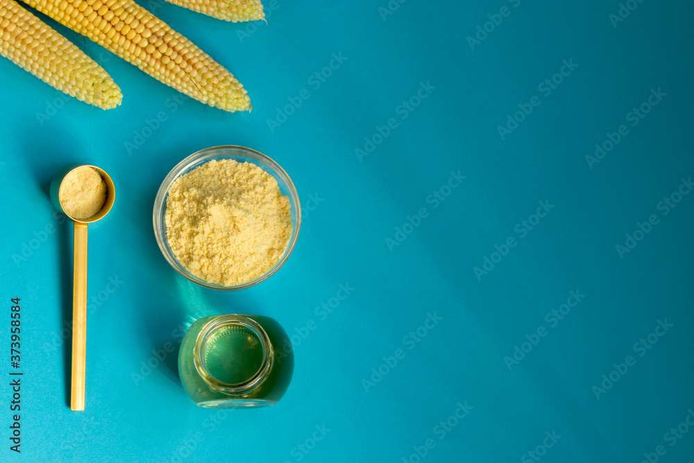 Corn oil and flour in a glass bowl, fresh corn on a blue background. The concept of the production of products from corn. Top view.