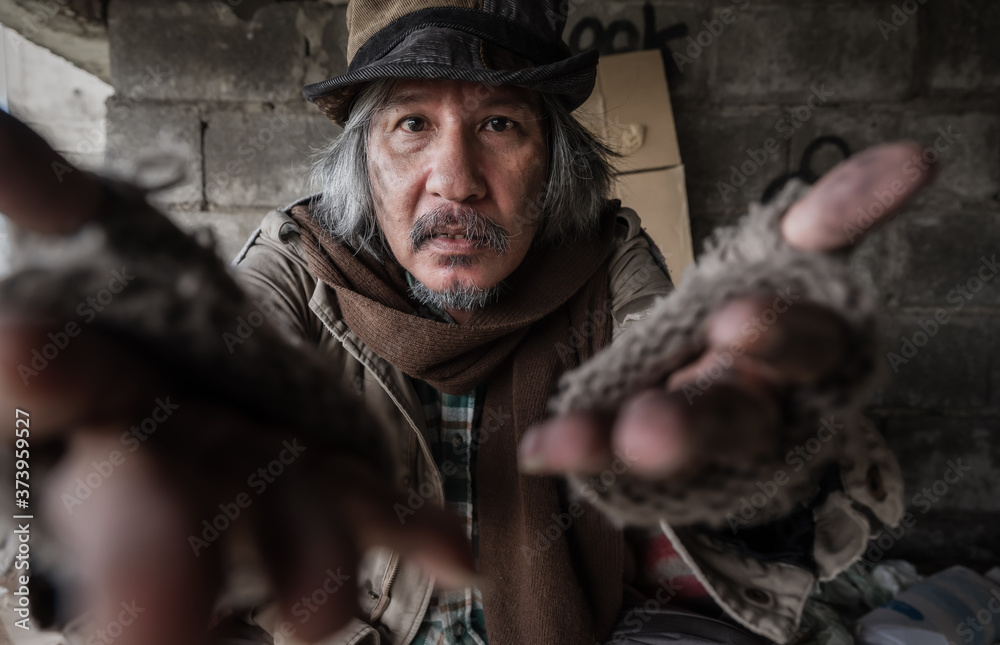 Old homeless man with gray beard wear gloves with sitting and hands up for asking help and food beggar because hungry. Closeup and focus to dirty face of poor man beggar. Help and hope concept.