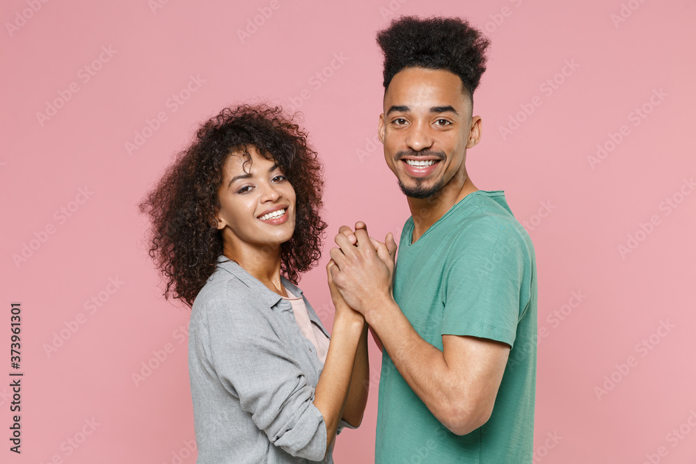 Side view of smiling young african american couple two friends guy girl in gray green casual clothes posing holding hands looking camera isolated on pastel pink color wall background studio portrait. Side view of smiling young african american couple two friends guy girl in gray green casual clothes posing holding hands looking camera isolated on pastel pink color wall background studio portrait.