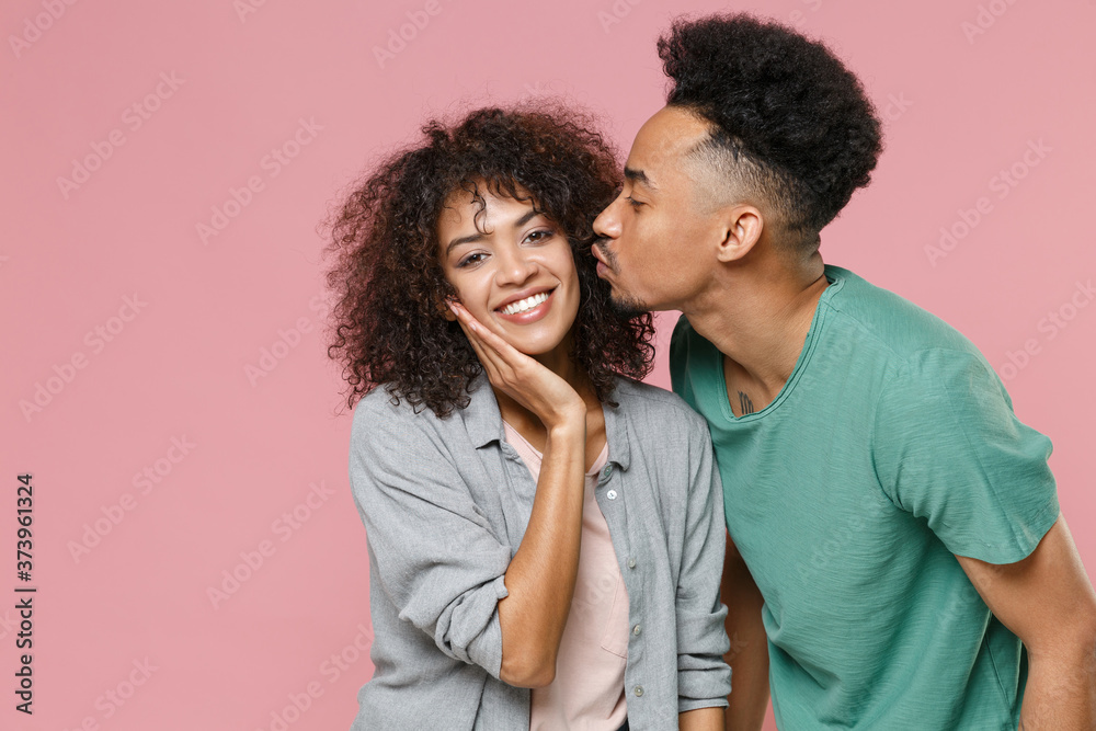 Smiling pretty cheerful young african american couple two friends guy girl in gray green casual clothes posing kissing put hand on cheek isolated on pastel pink color wall background studio portrait. Smiling pretty cheerful young african american couple two friends guy girl in gray green casual clothes posing kissing put hand on cheek isolated on pastel pink color wall background studio portrait.