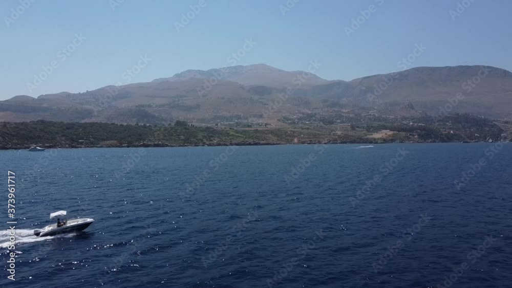 Speedboat Sailing At The Deep Blue Sea With Mountain Landscape On The Background In Scopello, Trapani In Sicily, Italy. - aerial drone shot Speedboat Sailing At The Deep Blue Sea With Mountain Landscape On The Background In Scopello, Trapani In Sicily, Italy. - aerial drone shot