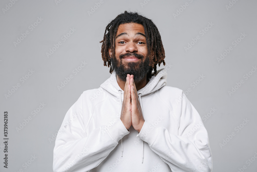 Pleading young african american man guy with dreadlocks 20s in white casual streetwear hoodie posing holding hands folded in prayer looking camera isolated on grey color background studio portrait. Pleading young african american man guy with dreadlocks 20s in white casual streetwear hoodie posing holding hands folded in prayer looking camera isolated on grey color background studio portrait.