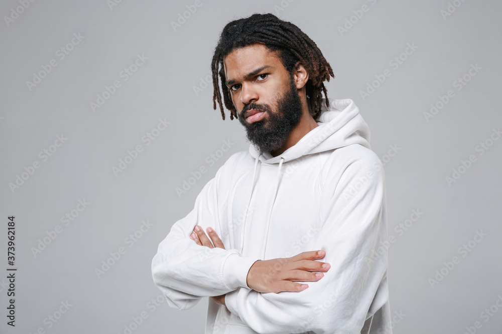 Side view of serious young african american man guy with dreadlocks 20s in white casual streetwear hoodie posing holding hands crossed looking camera isolated on grey color background studio portrait. Side view of serious young african american man guy with dreadlocks 20s in white casual streetwear hoodie posing holding hands crossed looking camera isolated on grey color background studio portrait.