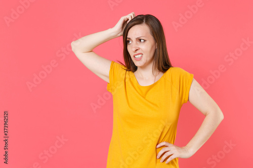 Preoccupied puzzled concerned confused young brunette woman 20s wearing yellow casual t-shirt posing standing looking aside put hand on head isolated on pink color wall background studio portrait.