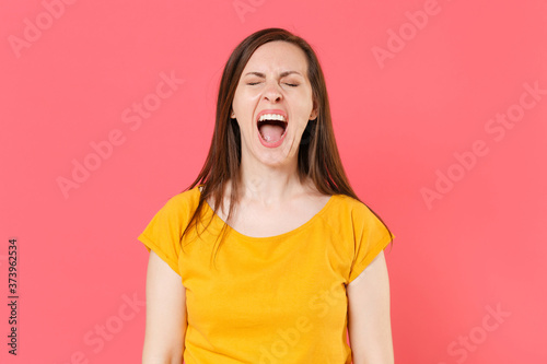 Crazy frustrated crying displeased young brunette woman 20s wearing yellow casual t-shirt posing standing screaming shouting keeping eyes closed isolated on pink color wall background studio portrait.