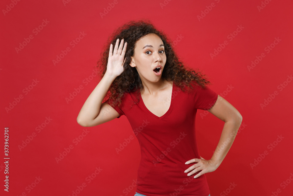Shocked young african american woman girl in casual t-shirt posing isolated on red background studio portrait. People lifestyle concept. Mock up copy space. Try to hear you overhear listen intently. Shocked young african american woman girl in casual t-shirt posing isolated on red background studio portrait. People lifestyle concept. Mock up copy space. Try to hear you overhear listen intently.