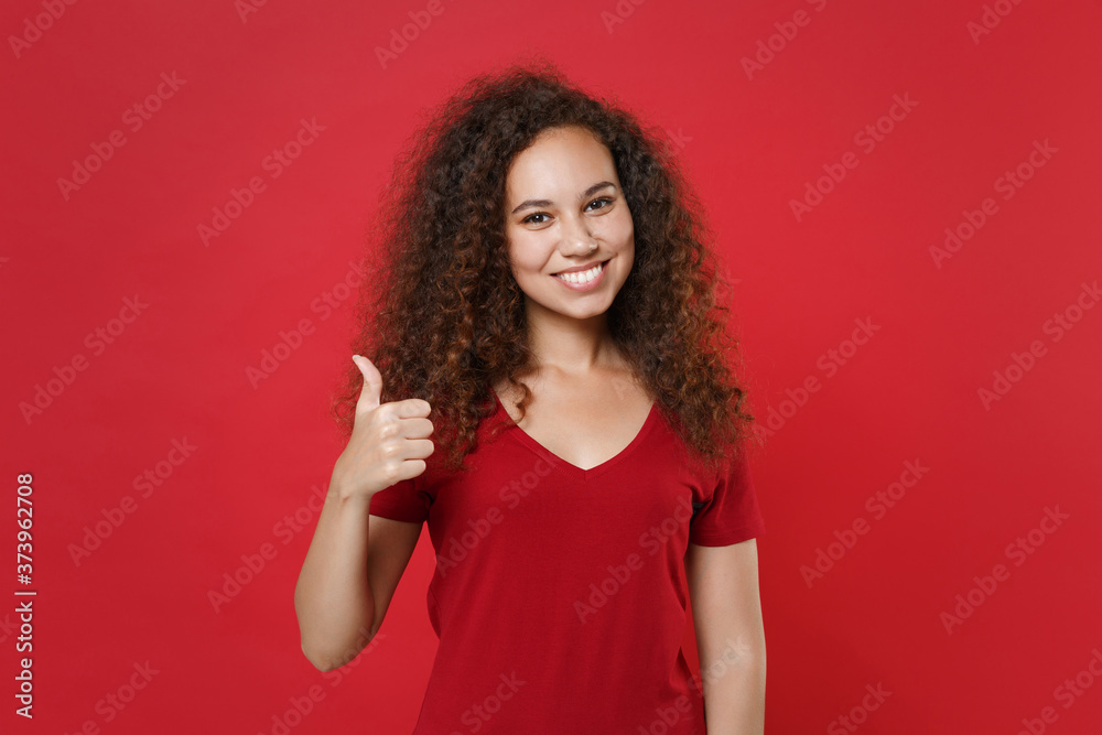 Smiling young african american woman girl in casual t-shirt posing isolated on bright red background studio portrait. People sincere emotions lifestyle concept. Mock up copy space. Showing thumb up. Smiling young african american woman girl in casual t-shirt posing isolated on bright red background studio portrait. People sincere emotions lifestyle concept. Mock up copy space. Showing thumb up.