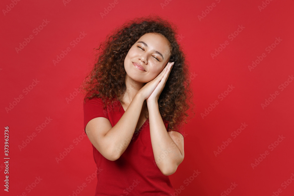 Smiling young african american woman girl in casual t-shirt posing isolated on red wall background studio portrait. People lifestyle concept. Mock up copy space. Sleep with folded hands under cheek. Smiling young african american woman girl in casual t-shirt posing isolated on red wall background studio portrait. People lifestyle concept. Mock up copy space. Sleep with folded hands under cheek.