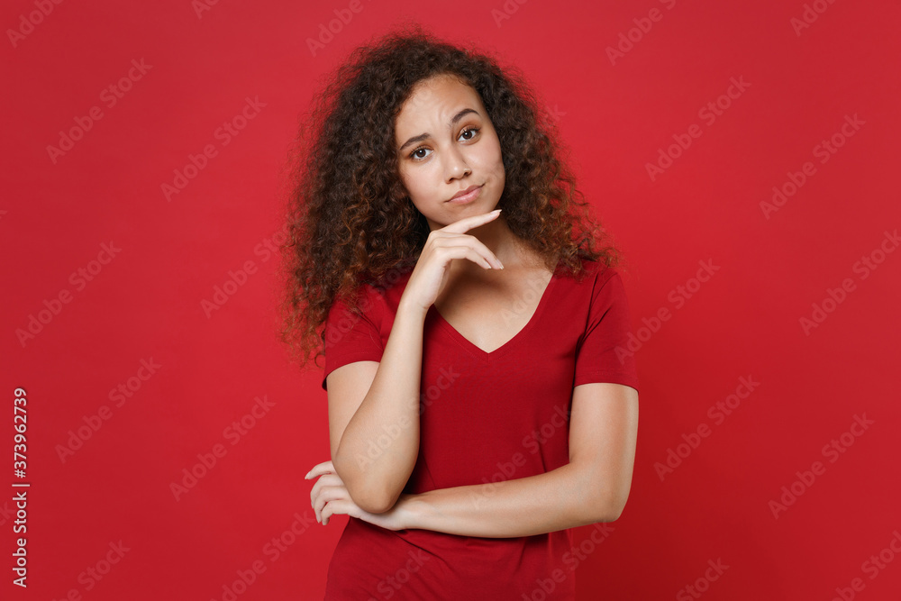Confused young african american woman girl in casual t-shirt posing isolated on red background studio portrait. People sincere emotions lifestyle concept. Mock up copy space. Put hand prop up on chin. Confused young african american woman girl in casual t-shirt posing isolated on red background studio portrait. People sincere emotions lifestyle concept. Mock up copy space. Put hand prop up on chin.