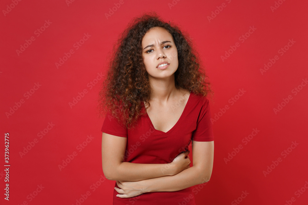 Sick young african american woman girl in casual t-shirt isolated on red background studio portrait. People lifestyle healthcare concept. Having abdominal pain put hold hands on stomach belly ache Sick young african american woman girl in casual t-shirt isolated on red background studio portrait. People lifestyle healthcare concept. Having abdominal pain put hold hands on stomach belly ache