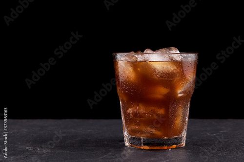 Iced coffee with ice in a transparent misted glass against a dark background with copy space. Close-up, selective focus