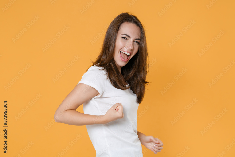 Side view of happy joyful young brunette woman 20s wearing white blank empty design casual t-shirt posing clenching fists doing winner gesture isolated on yellow color wall background studio portrait. Side view of happy joyful young brunette woman 20s wearing white blank empty design casual t-shirt posing clenching fists doing winner gesture isolated on yellow color wall background studio portrait.