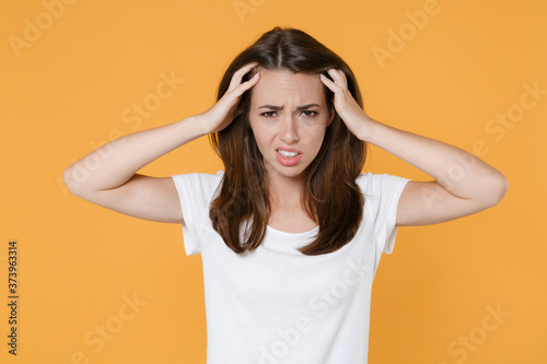 Preoccupied puzzled tired young brunette woman wearing white blank empty design casual t-shirt posing having headache put hands on head looking camera isolated on yellow background studio portrait.