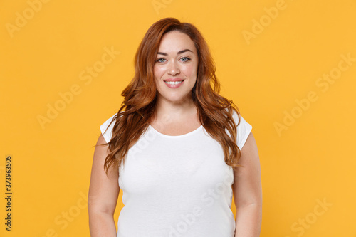 Cuadro en lienzo Smiling beautiful charming young redhead plus size body positive female woman girl 20s in white blank design casual t-shirt posing looking camera isolated on yellow color background studio portrait