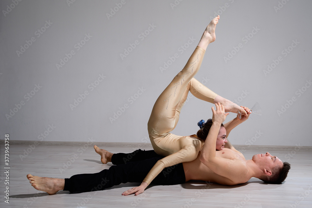 Acrobatic couple perform number on a white background. A duet of gymnasts rehearsing a performance with support. A man and a very flexible woman are dancing. Acrobatic couple perform number on a white background. A duet of gymnasts rehearsing a performance with support. A man and a very flexible woman are dancing.