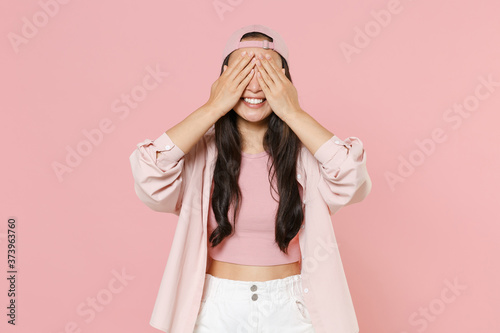 Smiling young asian woman girl in casual clothes cap posing isolated on pastel pink background studio portrait. People emotions lifestyle concept. Mock up copy space. Hiding, covering eyes with hands.