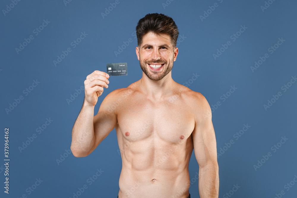 Smiling young bearded fitness sporty strong guy bare-chested muscular sportsman posing isolated on blue background studio portrait. Workout sport motivation lifestyle concept. Hold credit bank card. Smiling young bearded fitness sporty strong guy bare-chested muscular sportsman posing isolated on blue background studio portrait. Workout sport motivation lifestyle concept. Hold credit bank card.