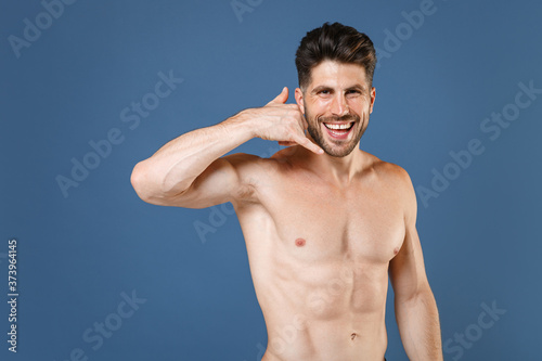 Cheerful young bearded fitness sporty strong guy bare-chested muscular sportsman isolated on blue background. Workout sport motivation lifestyle concept. Doing phone gesture like says call me back. © ViDi Studio