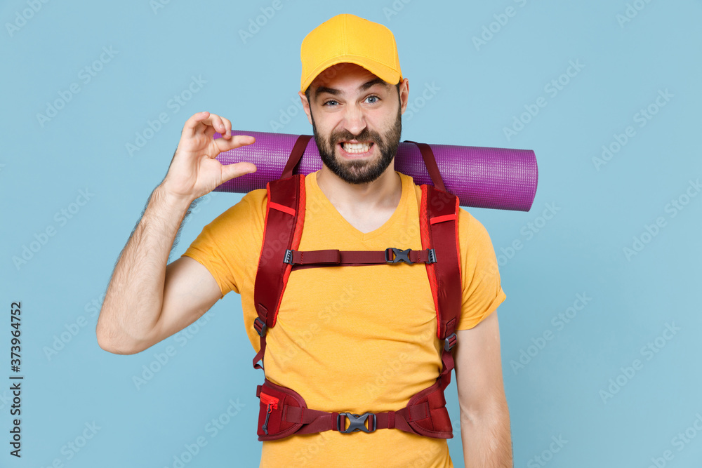 Confused traveler man in yellow t-shirt cap backpack isolated on blue background. Tourist traveling on weekend getaway. Tourism discovering hiking concept. Gesturing demonstrating size with workspace. Confused traveler man in yellow t-shirt cap backpack isolated on blue background. Tourist traveling on weekend getaway. Tourism discovering hiking concept. Gesturing demonstrating size with workspace.