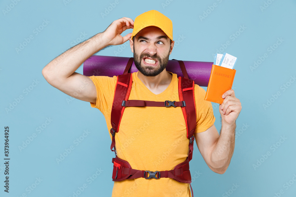 Puzzled traveler young man in t-shirt cap with backpack isolated on blue background. Tourist traveling on weekend getaway. Tourism discovering hiking concept. Hold passport tickets put hand on head.