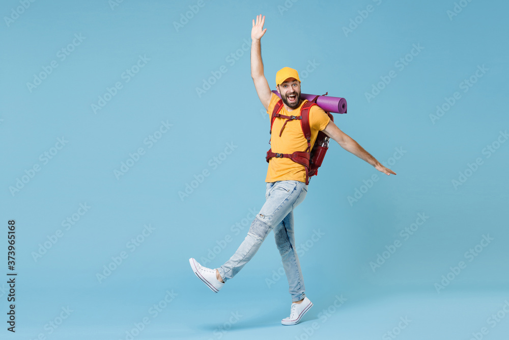 Full length portrait of excited young traveler man in t-shirt cap backpack isolated on blue background. Tourist traveling on weekend. Tourism discovering hiking concept. Rising spreading hands legs.
