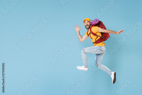 Full length portrait Excited young traveler man in cap with backpack isolated on blue wall background. Tourist traveling on weekend getaway. Tourism discovering hiking concept. Jumping like running.