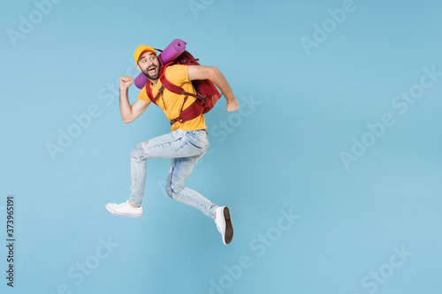 Full length portrait Amazed young traveler man in t-shirt cap with backpack isolated on blue background. Tourist traveling on weekend getaway. Tourism discovering hiking concept. Jumping like running.