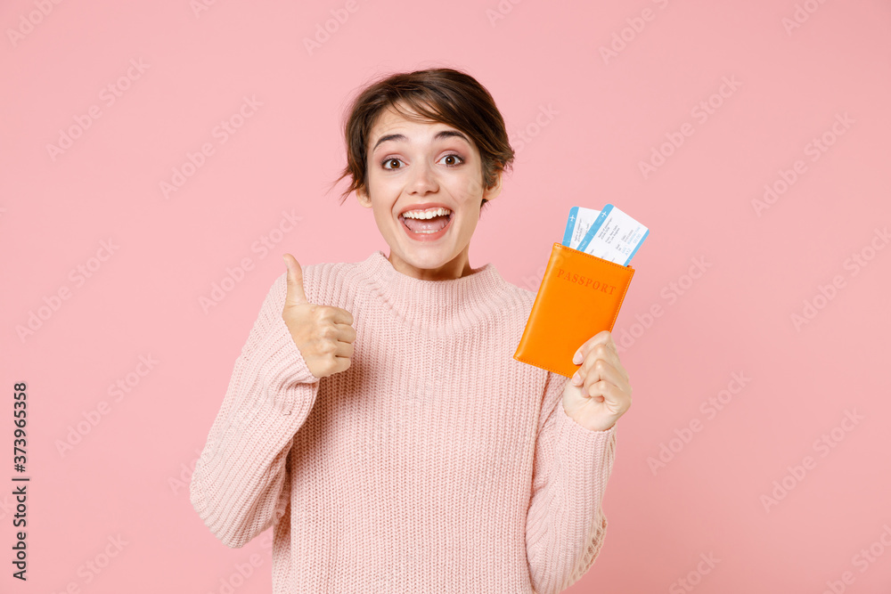Excited young woman in casual sweater isolated on pastel pink background. Passenger traveling abroad to travel on weekends getaway. Air flight journey concept. Hold passport tickets, showing thumb up. Excited young woman in casual sweater isolated on pastel pink background. Passenger traveling abroad to travel on weekends getaway. Air flight journey concept. Hold passport tickets, showing thumb up.