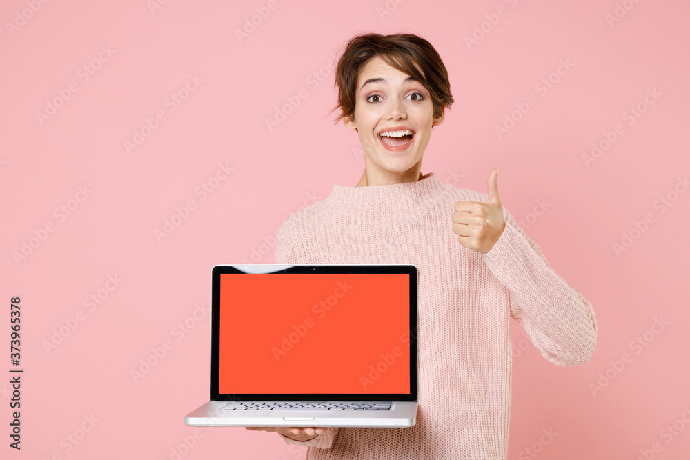 Excited young woman girl in knitted casual sweater isolated on pastel pink background. People lifestyle concept. Mock up copy space. Hold laptop pc computer with blank empty screen, showing thumb up. Excited young woman girl in knitted casual sweater isolated on pastel pink background. People lifestyle concept. Mock up copy space. Hold laptop pc computer with blank empty screen, showing thumb up.