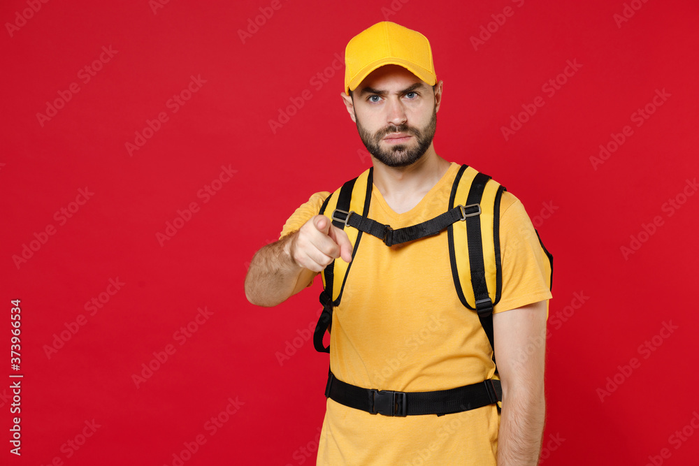Sad delivery employee man guy 20s in yellow cap t-shirt uniform thermal bag backpack with food work as courier isolated on red background studio. Service during quarantine coronavirus covid-19 virus. Sad delivery employee man guy 20s in yellow cap t-shirt uniform thermal bag backpack with food work as courier isolated on red background studio. Service during quarantine coronavirus covid-19 virus.