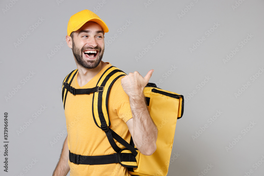 Delivery employee man guy in yellow cap t-shirt uniform thermal food bag backpack work courier service during quarantine covid-19 virus pointing fingers on workspace isolated on gray background studio Delivery employee man guy in yellow cap t-shirt uniform thermal food bag backpack work courier service during quarantine covid-19 virus pointing fingers on workspace isolated on gray background studio