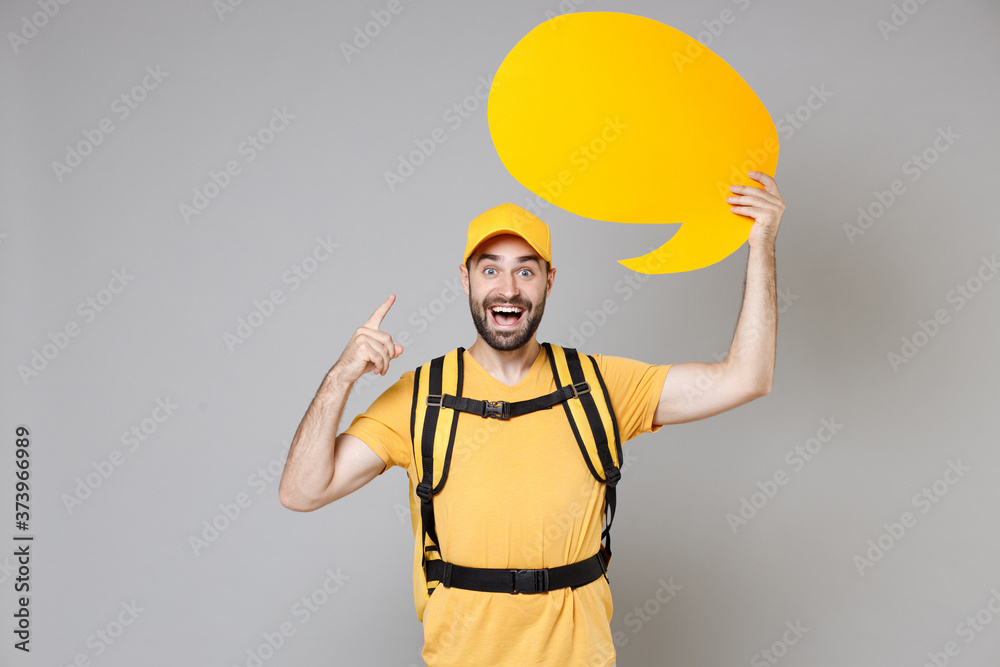 Delivery employee man guy male in yellow cap t-shirt uniform thermal food bag backpack work courier service during quarantine coronavirus covid-19 hold speech bubble isolated on gray background studio Delivery employee man guy male in yellow cap t-shirt uniform thermal food bag backpack work courier service during quarantine coronavirus covid-19 hold speech bubble isolated on gray background studio