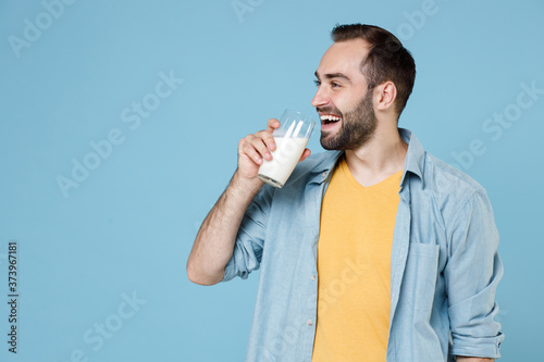 Photos Smiling cheerful handsome young bearded man guy 20s wearing casual clothes posing holding in hand glass drinking milk looking aside isolated on pastel blue color wall background studio portrait