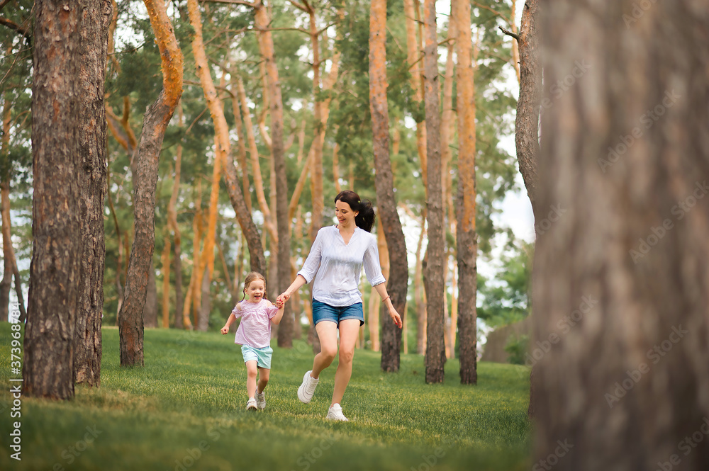Fototapeta premium Mom and daughter are running in the forest close-up and copy space. The sisters are playing hide and seek in the forest. Mother's day, women's holiday.