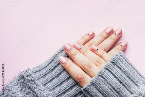 Female hands in a gray fluffy knitted sweater with trendy beautiful manicure - pink nude nails with black small dots on a pink background with copy space