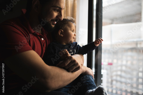 Father plays with his little boy less than a year by the window