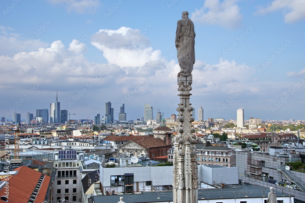 Obraz premium Statue on spire of Milan Cathedral on blue sky background, Milan, Italy. Detail of Gothic roof overlooking Milano city in summer. Nice view of Milan from above