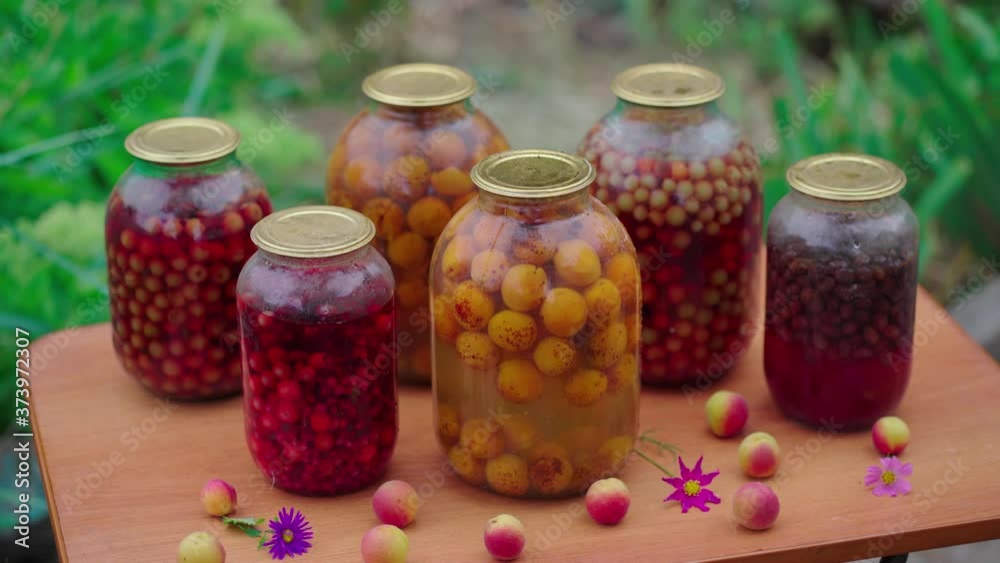 Jars with compote on table. Sealed glass jars with kompot placed on table near flowers and fruits on summer day in garden Jars with compote on table. Sealed glass jars with kompot placed on table near flowers and fruits on summer day in garden