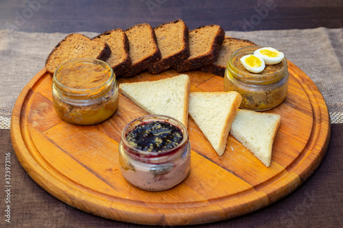 Fresh homemade pate in glass jars on a wooden tray with rye and white bread. Liver, meat pate decorated with eggs. Homemade breakfast or snack. close up view