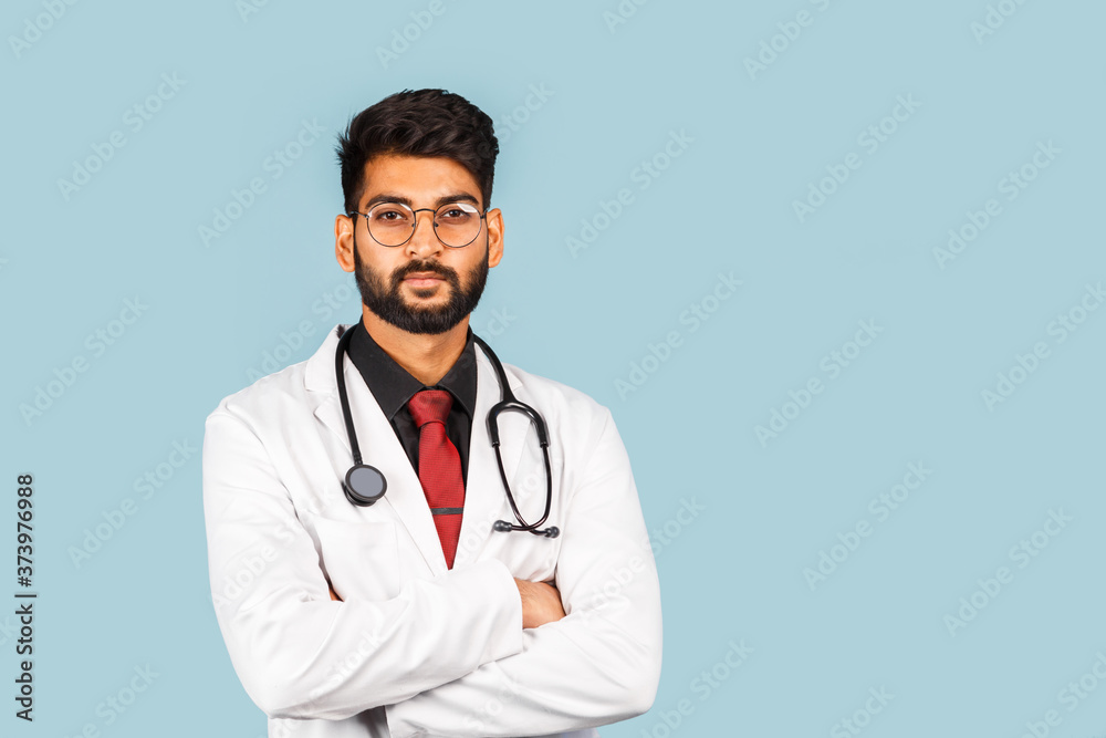 Cute Indian / Asian doctor wearing glasses with stethoscope, tie and white coat on light blue background.