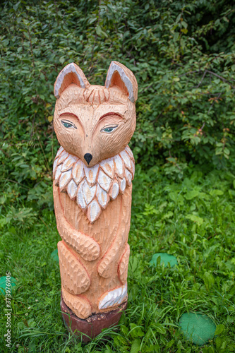 the figure of a fox carved from wood on a background of green forest