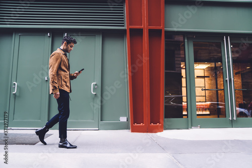 Young man in trendy clothes walking and using smartphone on stret photo