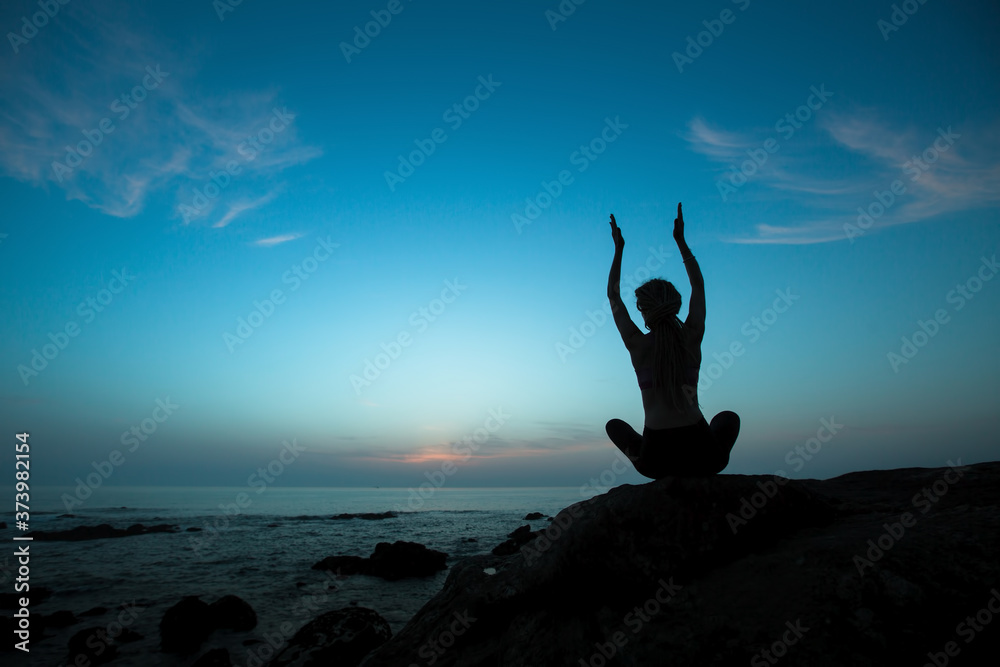 Silhouette of yoga woman on the beach in the twilight.