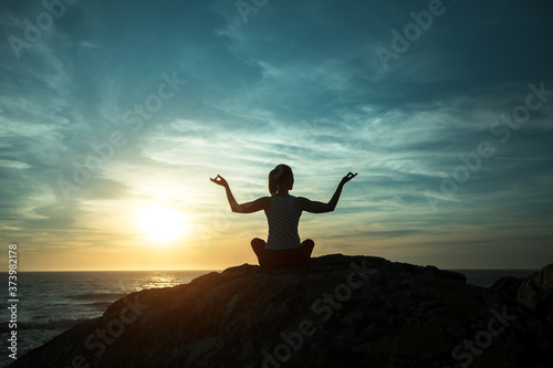 Silhouette of Yoga woman sitting in Lotus position on the ocean beach during sunset.