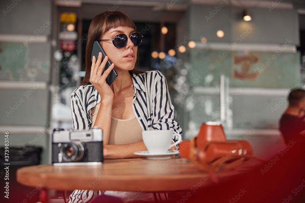 Female in sunglasses is talking on smartphone and is waiting for somebody