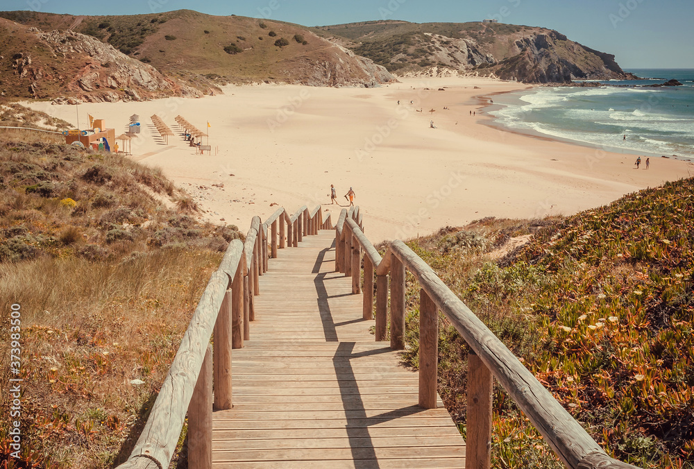 Sunny beach with relaxed people in rural landscape of Portugal. Ocean waters and green hills over peaceful seaside